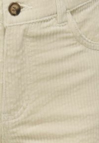 Primer plano de pantalones de pana beige que muestra el bolsillo frontal, el lazo del cinturón, los detalles de la costura y un botón marrón.