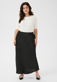 Jupe maxi noire avec une texture lisse et fluide, associée à un haut ajusté en maille blanche. Comprend une taille élastique simple. Chaussures noires brillantes.