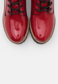 Bottes en cuir verni rouge avec une finition brillante, bout rond, lacets noirs et surpiqûres contrastantes marron le long de la semelle.