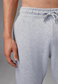 Pantalones de chándal gris claro con una textura suave, cintura elástica y detalle de cordón. Ajustados en la cintura, con un corte suelto a lo largo de las piernas.