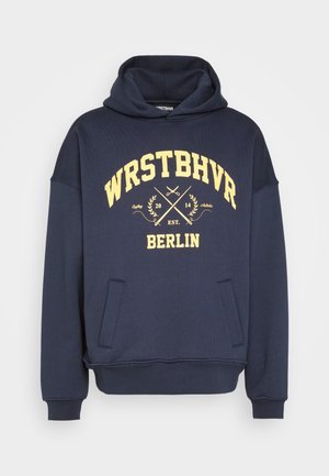 Granatowa bluza z kapturem z przednimi kieszeniami, żółtym napisem "WRSTBHVR BERLIN", grafiką skrzyżowanych nożyczek oraz kapturem bez sznureczków.