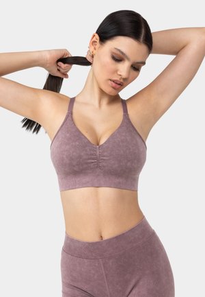 Mauve sömlös sport-bh med breda axelremmar, v-ringning, subtil textur och rynkad detalj i mitten, i kombination med matchande leggings.