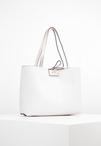 Sac fourre-tout blanc texturé avec accents argentés et doubles anses. Présente un design minimaliste et une fermeture éclair en haut.