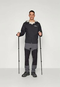Black waterproof jacket with gray accents, paired with gray pants featuring darker knee patches; includes adjustable poles and boots.