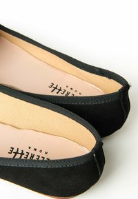 Ballerine in suede nero con fodera beige liscia, punta arrotondata e un sottile bordo nero lungo il bordo.