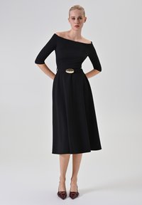 Schwarzes Off-Shoulder-Kleid mit dreiviertel Ärmeln, definiertem Taillieren und einer goldenen ovalen Gürtelschnalle; glattes Material mit einem fließenden A-Linien-Rock.