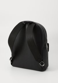Svart ryggsäck med en texturerad yta, böjd form, justerbara tygremmar och en sidodragkedja. Minimalistisk design utan mönster.