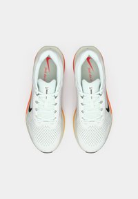 Zapatillas deportivas blancas con parte superior de malla, logo Swoosh negro y acentos naranjas en la suela. Incluyen cordones y lengüeta acolchada.