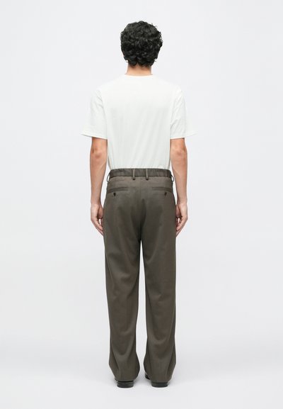 Férfi öltözet, amely egy testhezálló fehér pólót és laza szabású, sötétzöld nadrágot tartalmaz, amelynek két hátsó zsebe és sima textúrája van.