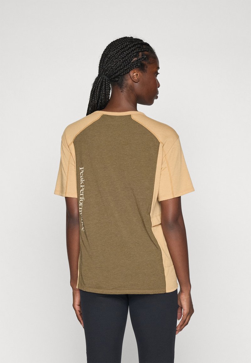 Kortermet t-skjorte i olivengrønn og beige farger, myk tekstur og en vertikal "Peak Performance" logo langs siden.