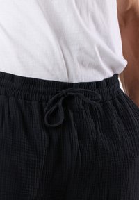 Sorte, strukturerede drawstring-bukser med en samlet talje og subtile lodrette striber. Sammen med en ensfarvet hvid top.