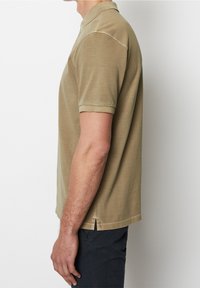 Pohodlné polo tričko s krátkým rukávem v khaki barvě, vyrobené z měkké tkaniny. Disponuje klasickým límcem a postranními rozparky pro větší pohodlí. Jednoduchý design s čistými liniemi.