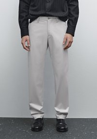 Beige Anzughosen mit einer glatten Textur, tailliertem Schnitt, seitlichen Taschen und geradem Bein, kombiniert mit schwarzen Dressschuhen.