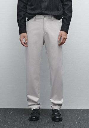 Beige dress pants with a smooth texture, tailored fit, side pockets, and a straight-leg design, paired with black dress shoes.