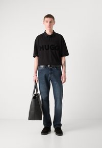 Juoda polo marškinėliai su "HUGO" logotipu, mėlynų džinsų kelnės, juodas diržas, juoda rankinė ir tamsi avalynė. Paprastas dizainas, laisvas fasonas.