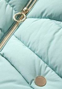 Tissu matelassé bleu clair avec fermeture éclair dorée et détail de bouton rond en métal sur une veste ou un manteau.