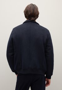 Marineblaue Fleecejacke mit Kragen, gerippten Bündchen und Saum. Verfügt über eine glatte Textur und minimale Nähte, entworfen für legere Kleidung.