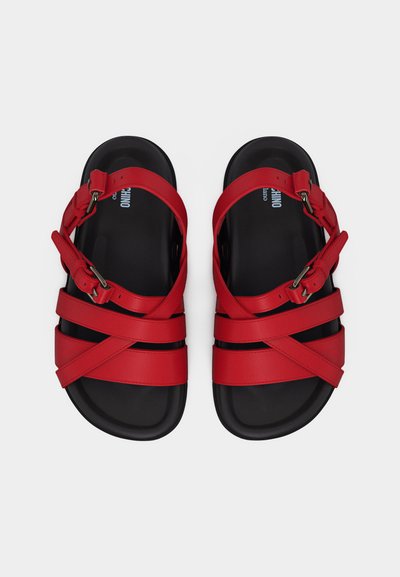 Paire de sandales noires avec des brides croisées rouges et des boucles réglables, vues de dessus sur un fond blanc.