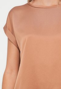 Krátký rukáv, růžový top s hladkou, matnou texturou a kulatým výstřihem. Otočené rukávy dodávají designu jemný detail.