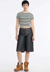 Gestreepte crop top in lichtblauw en zwart, gecombineerd met donkere denim culottes en tan laarzen. Zichtbare stiksels en knoopaccenten.