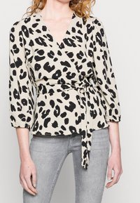 Blusa avvolgente con stampa leopardata in beige e nero, caratterizzata da un profondo scollo a V, maniche a palloncino a ¾ e dettaglio in vita con nodo. Tessuto morbido e fluido.