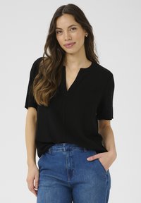 Svart kortärmad topp med avslappnad passform, V-ringning och mjukt material, i kombination med blå högmidjade jeans. Enkel och mångsidig design.