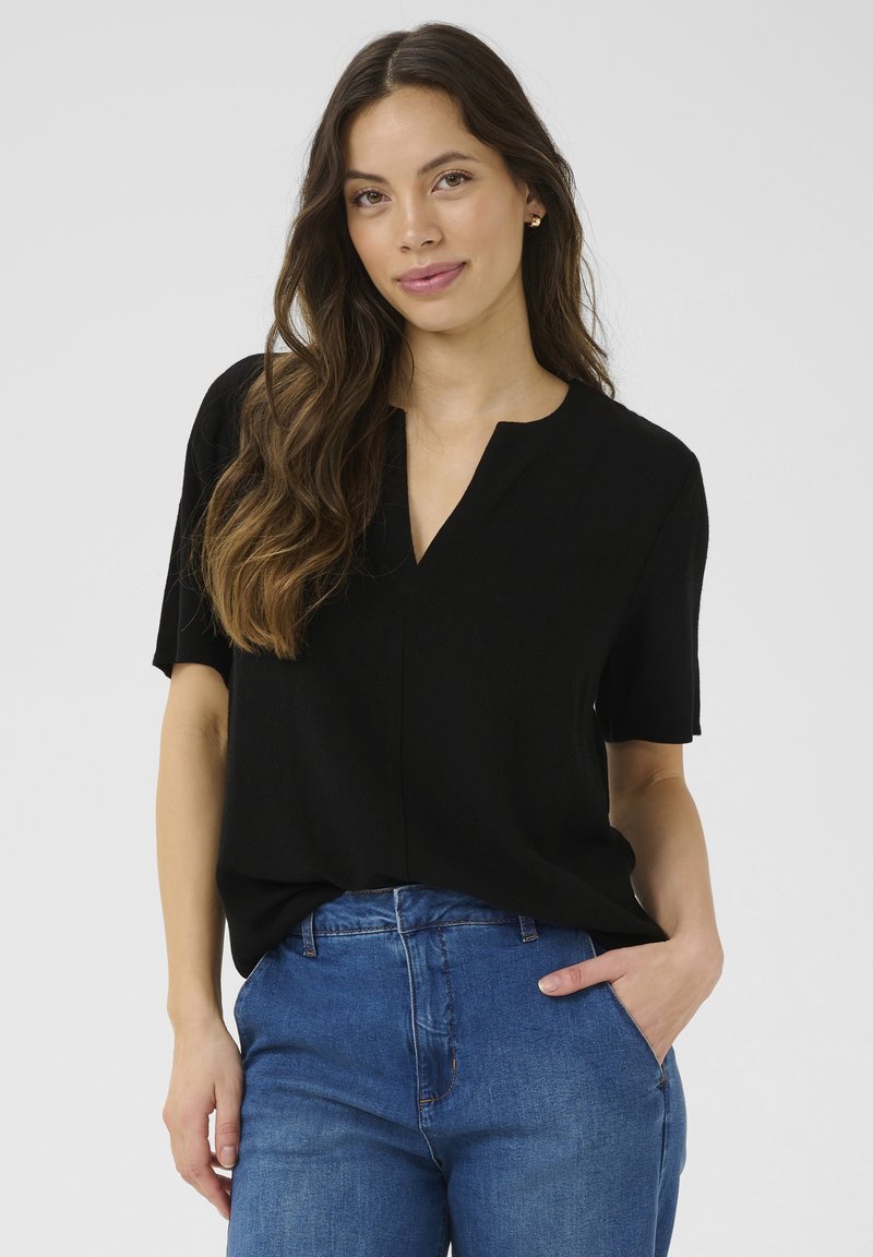 Svart kortärmad topp med avslappnad passform, V-ringning och mjukt material, i kombination med blå högmidjade jeans. Enkel och mångsidig design.