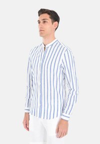 Camicia in lino a righe con righe verticali blu e bianche, colletto alla coreana, chiusura con bottoni e maniche lunghe. Tessuto liscio e vestibilità su misura.
