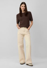 Haut à manches courtes côtelé marron associé à un pantalon large crème et des chaussures de couleur claire. Design simple, couleurs unies, coupe décontractée.