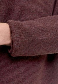 Maglione a maglia color bordeaux caratterizzato da un tessuto testurizzato con dettagli a costine sui polsi. Il primo piano mette in evidenza la sua morbidezza e il colore ricco.