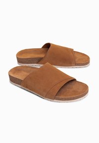 Paire de sandales slides en daim marron avec larges brides et semelle style liège sur fond blanc.