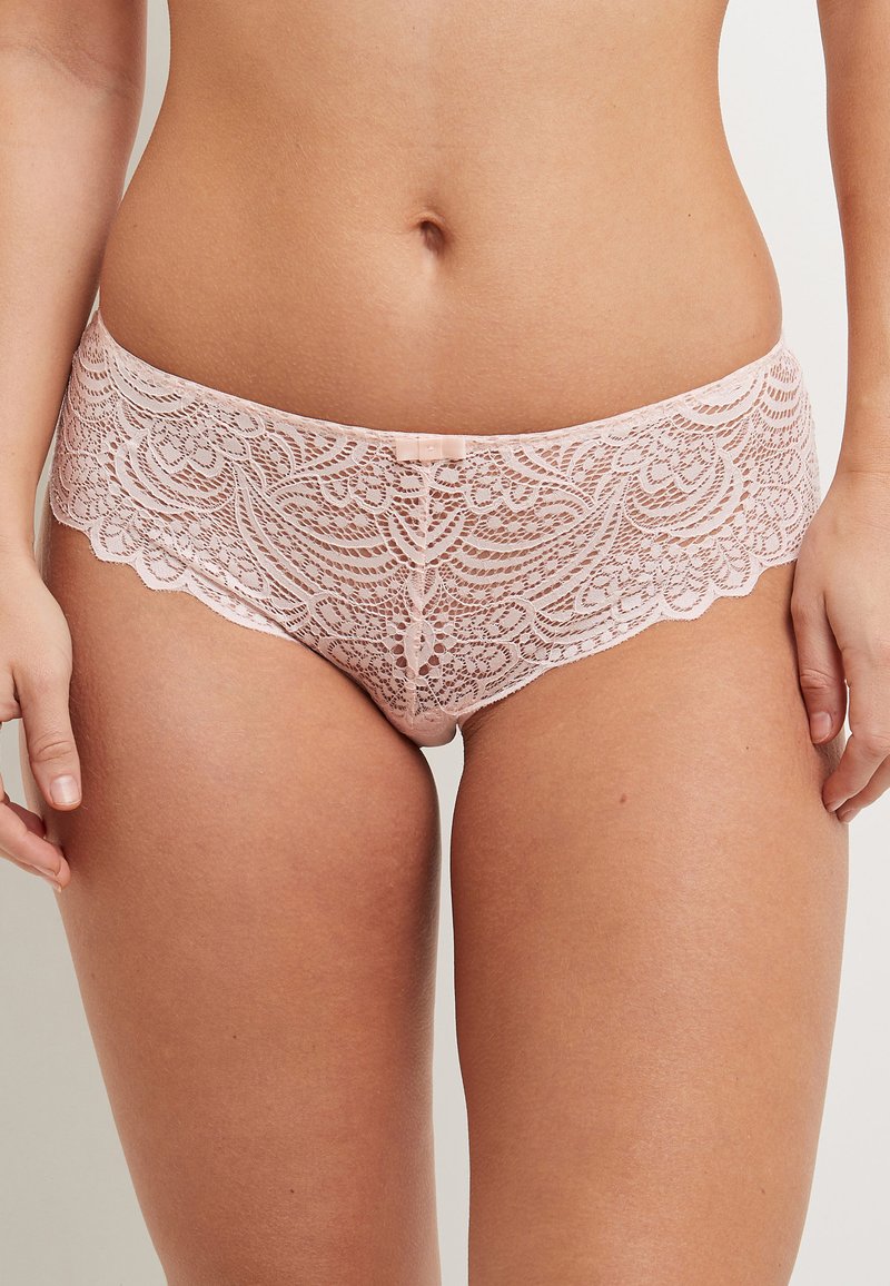 Le mutande hipster in pizzo rosa chiaro presentano un design con bordo scallopato e un sottile dettaglio a fiocco sul davanti, mettendo in risalto delicati motivi in pizzo.