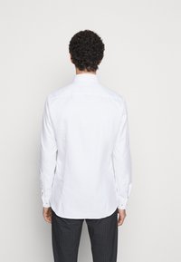 Biała koszula z długim rękawem, klasycznym kołnierzykiem i zapięciem na guziki. Gładka faktura i dopasowany krój, w zestawieniu z ciemnymi, wzorzystymi spodniami.