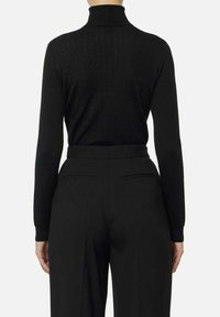 Maglione nero a collo alto con trama a coste e design aderente, abbinato a pantaloni neri sartoriali con due tasche sul retro.