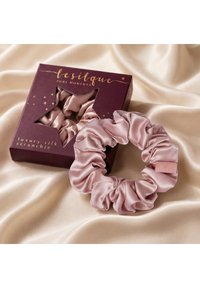 Chouchou en soie rose de luxe à côté d'un chouchou assorti dans une boîte violet foncé en forme d'étoile avec fenêtre, sur un fond en tissu de soie beige.