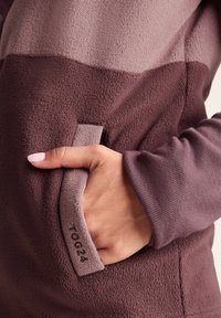 Fleece pullover in shades of mauve and plum with a textured finish. Features a side pocket and ribbed sleeve cuffs. Tag reads "TOG24."