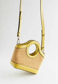 Sac à main jaune avec une anse ronde, texture tissée et contour noir. Bandoulière réglable et base structurée. Design moderne et unique.