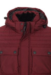 Burgundy puffjacka med huva, med en kviltad design, svart foder, två framfickor med lock och en central dragkedja.