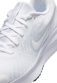 Chaussure de sport blanche présentant une tige en mesh texturé, des lacets plats, un col rembourré, et une semelle intermédiaire blanche avec des accents de semelle extérieure en caoutchouc noir.