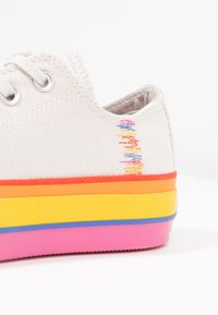 Leichte graue Canvas-Sneaker mit mehrfarbigem gestreiftem Sohlenrand, der rosa, gelbe, orange und blaue Schichten aufweist. Enthält einfarbige Nähte.