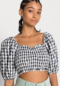 Top cropped em preto e branco com padrão quadriculado, mangas bufantes e detalhes franzidos. Apresenta accents florais e um decote ondulado.
