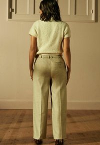 Lys grønne vide bukser med en subtil tekstur og bæltestropper, parret med en kortærmet hvid, fluffy sweater.