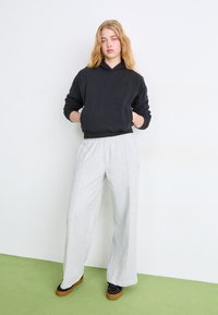 Sudadera negra con un corte relajado y puños acanalados, combinada con pantalones de chándal de pierna ancha en gris claro, que cuentan con una cinturilla elástica y una textura suave.