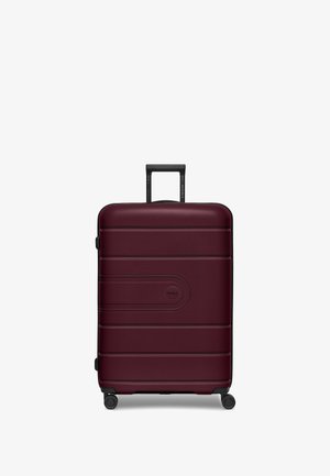 Valise rigide bordeaux avec une finition texturée, dotée d'une poignée noire rétractable et de quatre roues pivotantes pour une meilleure mobilité.