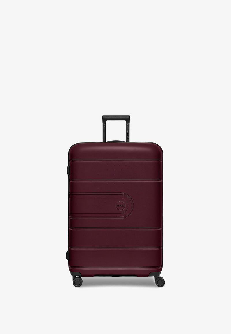 Valigia rigida color amaranto con finitura texture, dotata di manico nero retrattile e quattro ruote girevoli per una facile mobilità.