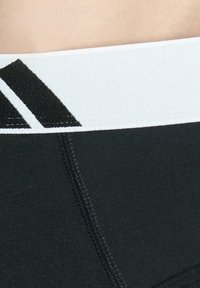 Schwarzer Sportbund mit weißen Streifen. Besitzt eine glatte Textur und tonale Nähte, die eine enge Passform betonen.