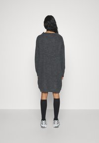 Robe-pull en maille gris foncé, longueur mi-cuisse, coupe oversize, texture côtelée, manches longues, portée avec des chaussettes noires montant jusqu'aux genoux et des baskets de sport.
