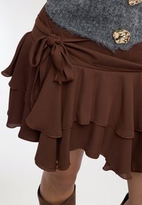 Gonna marrone a strati con orlo ondulato, caratterizzata da un laccio laterale e cuciture a contrasto. Tessuto morbido e leggero con una texture liscia.