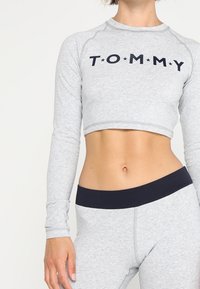 Graues, tailliertes Langarmoberteil mit dem Aufdruck "TOMMY" in Marineblau, kombiniert mit passenden grauen, hoch geschnittenen Leggings mit einem marineblauen Bund.