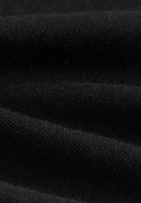Zwarte stof met een textuur en zichtbare ribbels, die zacht valt met subtiele variaties in schaduw en een licht fuzzy uitstraling.